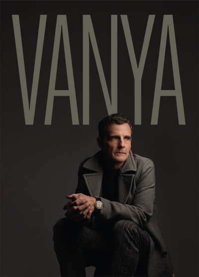 A man sits in the foreground of a dark space, his arm bent across a knee while he gazes off-frame. The letters behind him spell out "Vanya".