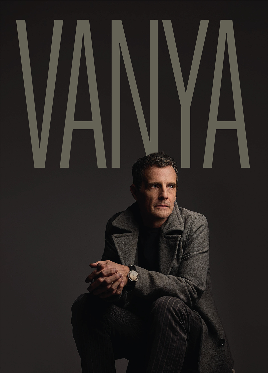 A man sits in the foreground of a dark space, his arm bent across a knee while he gazes off-frame. The letters behind him spell out "Vanya".